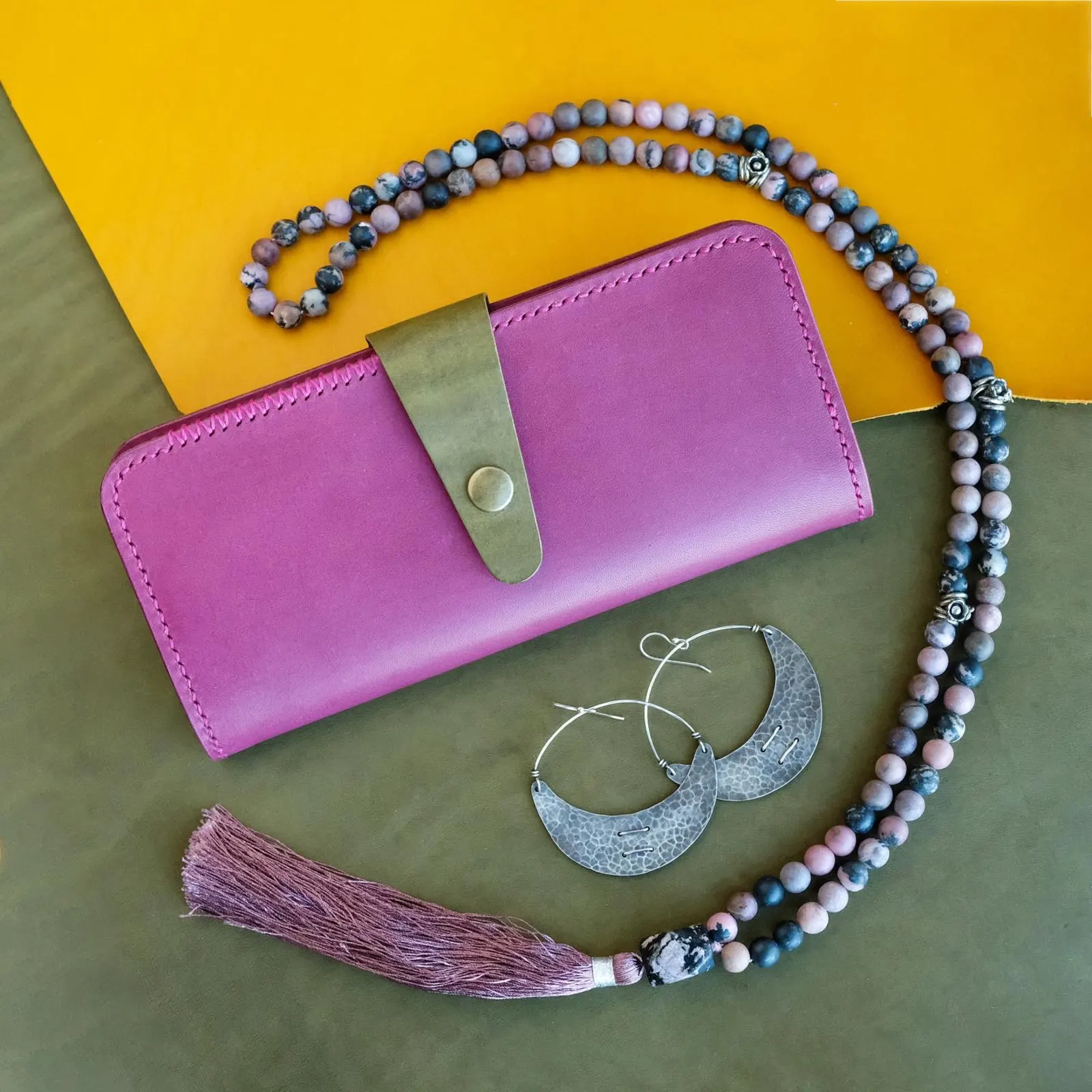 The Marina long wallet in purple leather styled with beaded jewelry on an olive backdrop