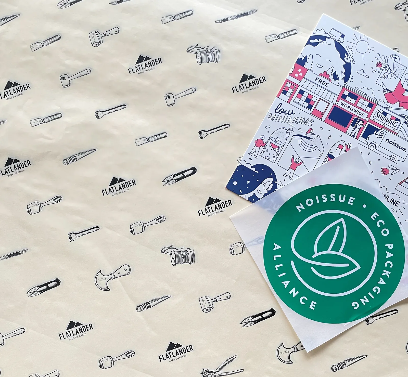 Custom tissue paper printed with leatherworking-tool illustrations and the Flatlander mark, shown with noissue compostable packaging