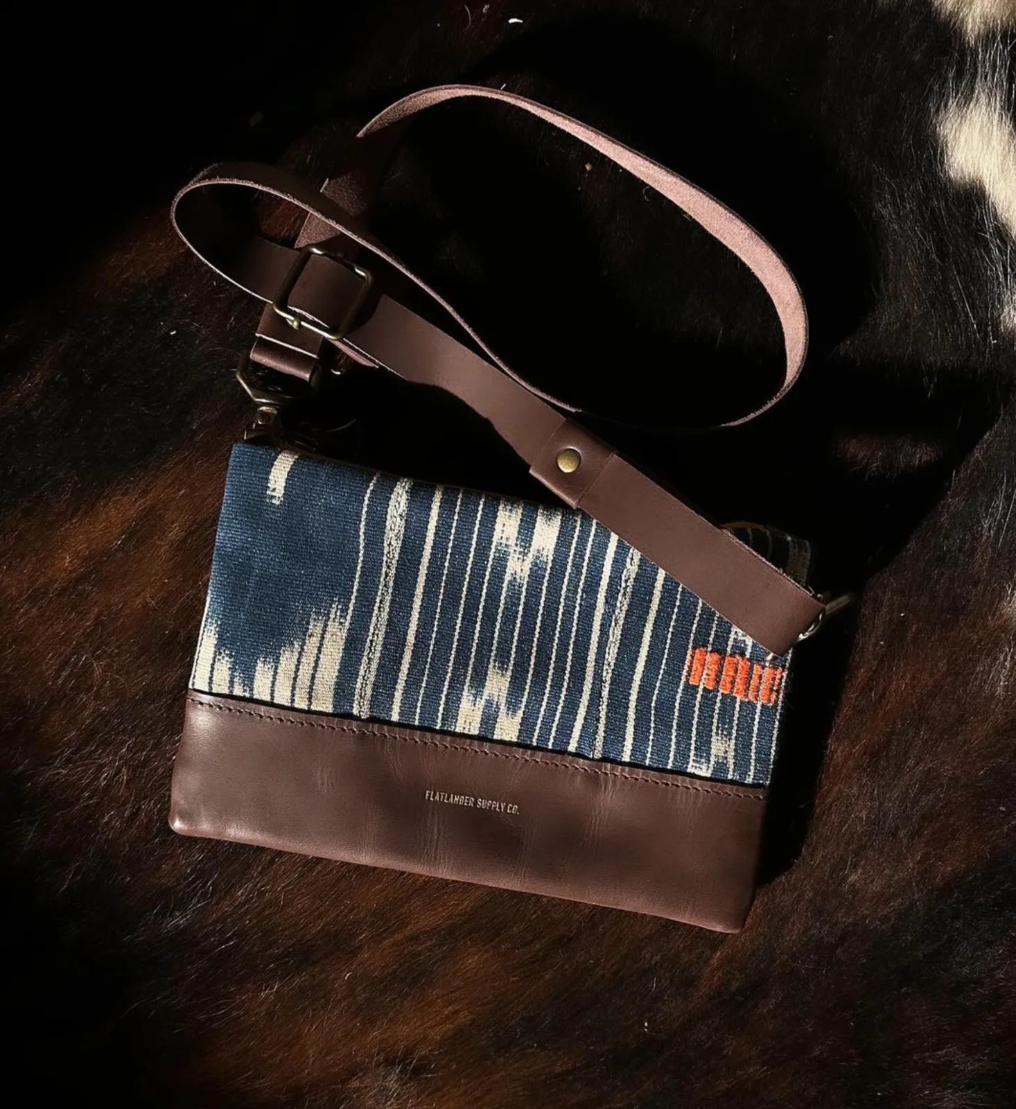 A crossbody bag pairing indigo ikat textile with a brown leather base, on a hide backdrop