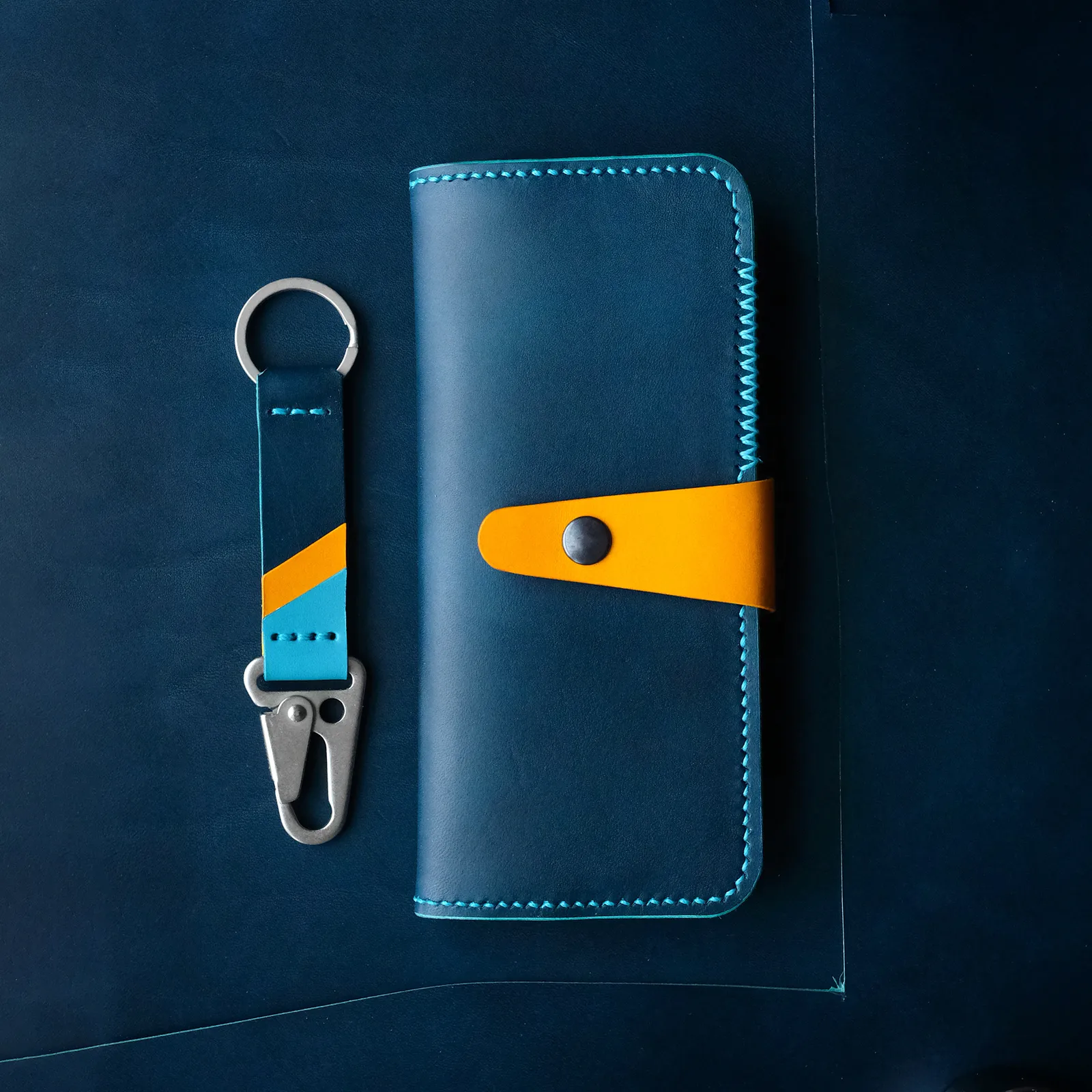 The Marina long wallet in navy leather with a yellow snap strap, beside a matching keychain