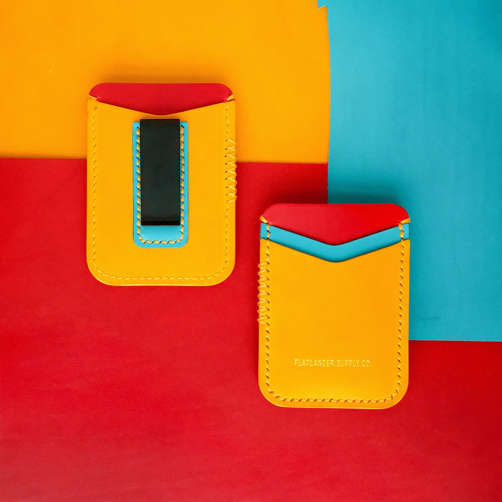 Two yellow money clips with cyan and red interiors on a red and cyan color-blocked backdrop