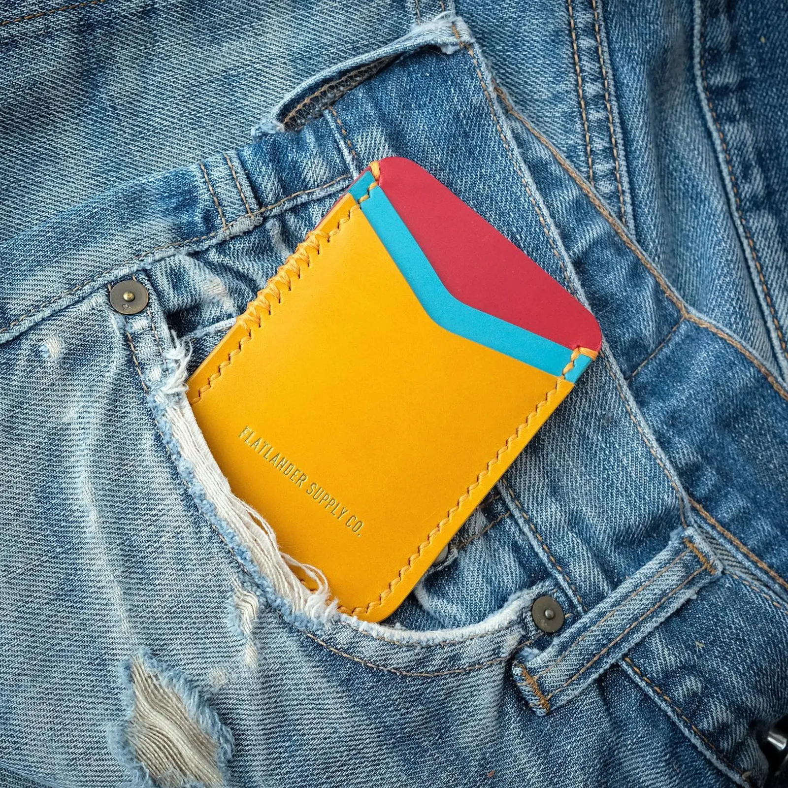 A yellow card sleeve with red and cyan contrast panels tucked into the back pocket of worn denim