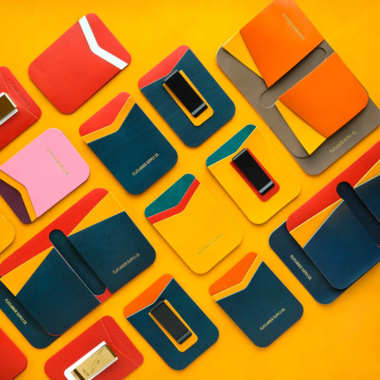 Fifteen card sleeves and money clips in every colorway, arranged in a loose grid on a yellow leather hide