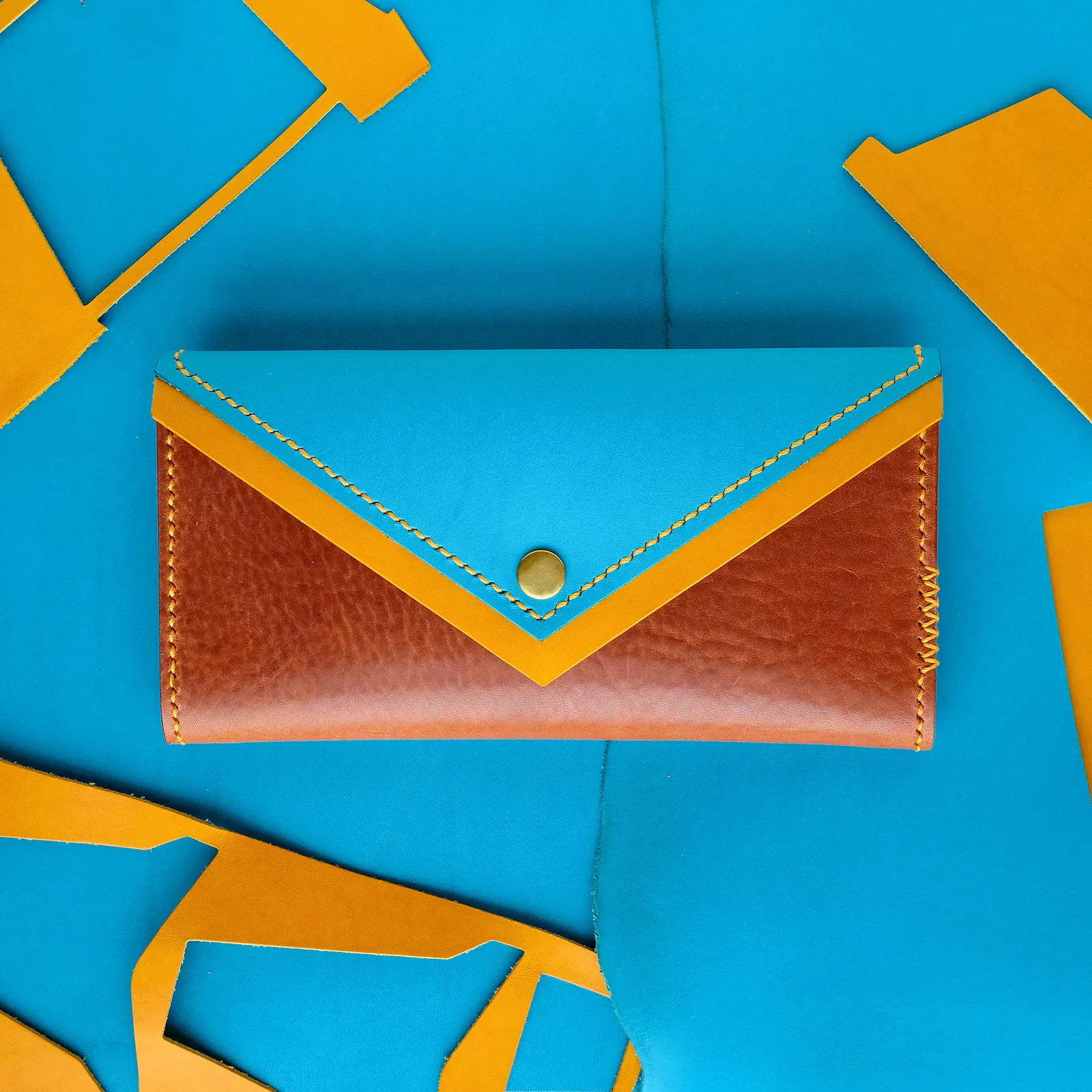 A tan and cyan envelope clutch on a cyan leather hide surrounded by leather offcuts