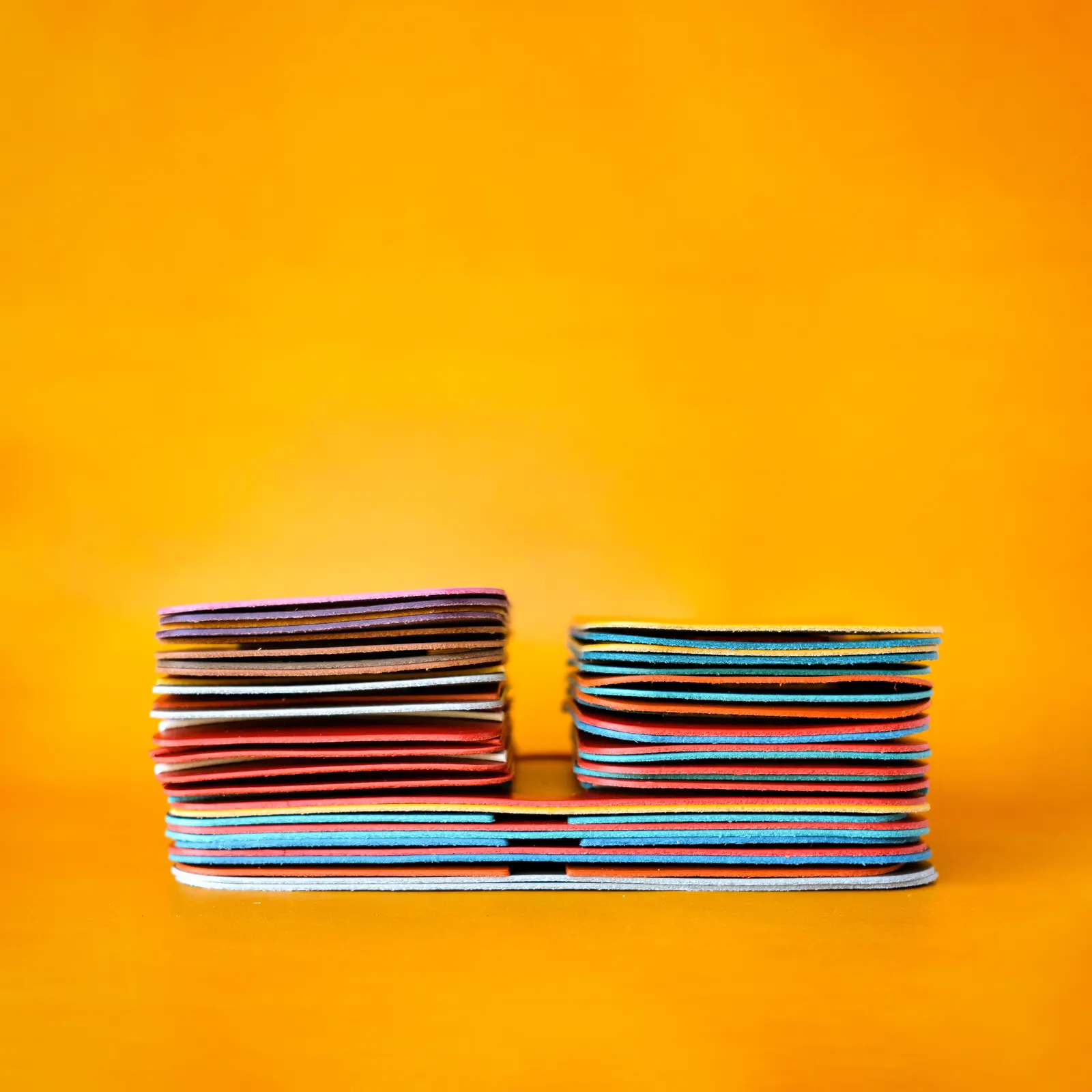 Two stacks of dyed leather panels photographed edge-on against yellow, showing the striped colored edges