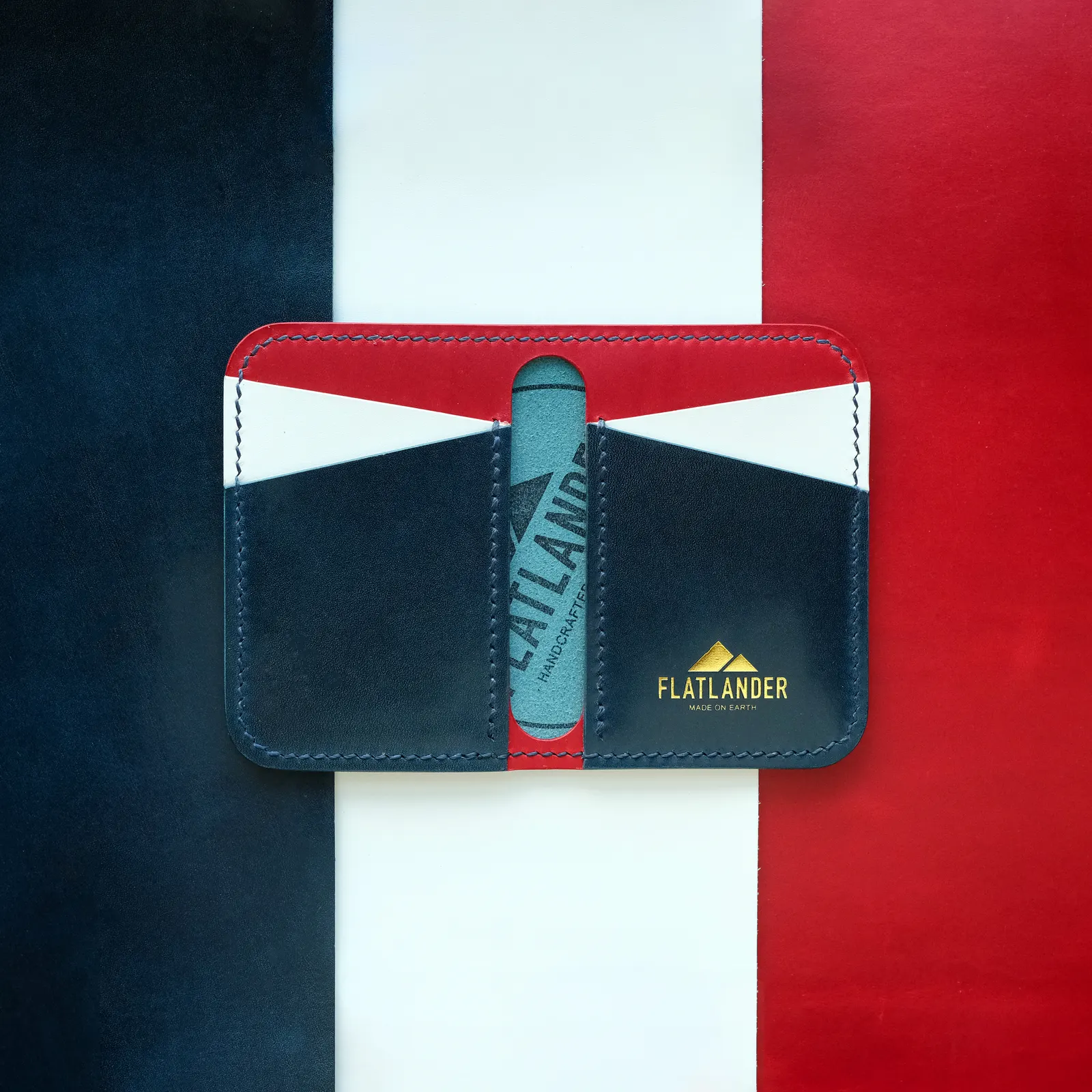 A navy bifold wallet with red and cyan panels, held against a red and white color-blocked backdrop