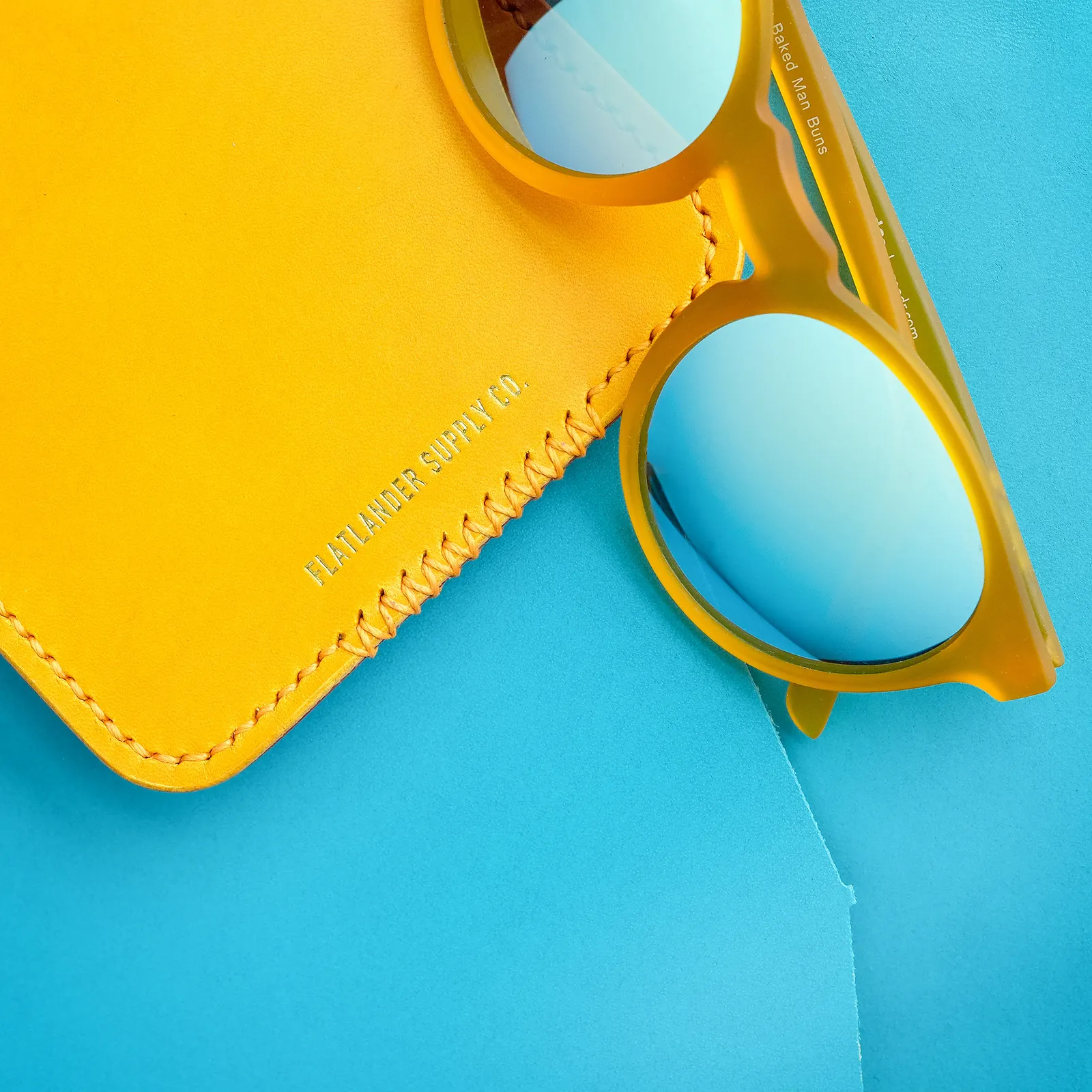 A yellow card sleeve and yellow sunglasses on a cyan leather hide