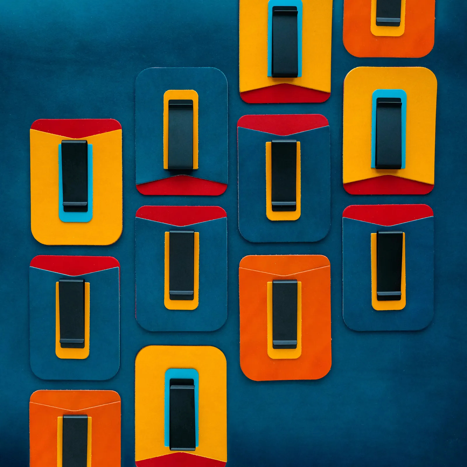 Money clips in orange, yellow and red laid out in a grid on deep blue leather