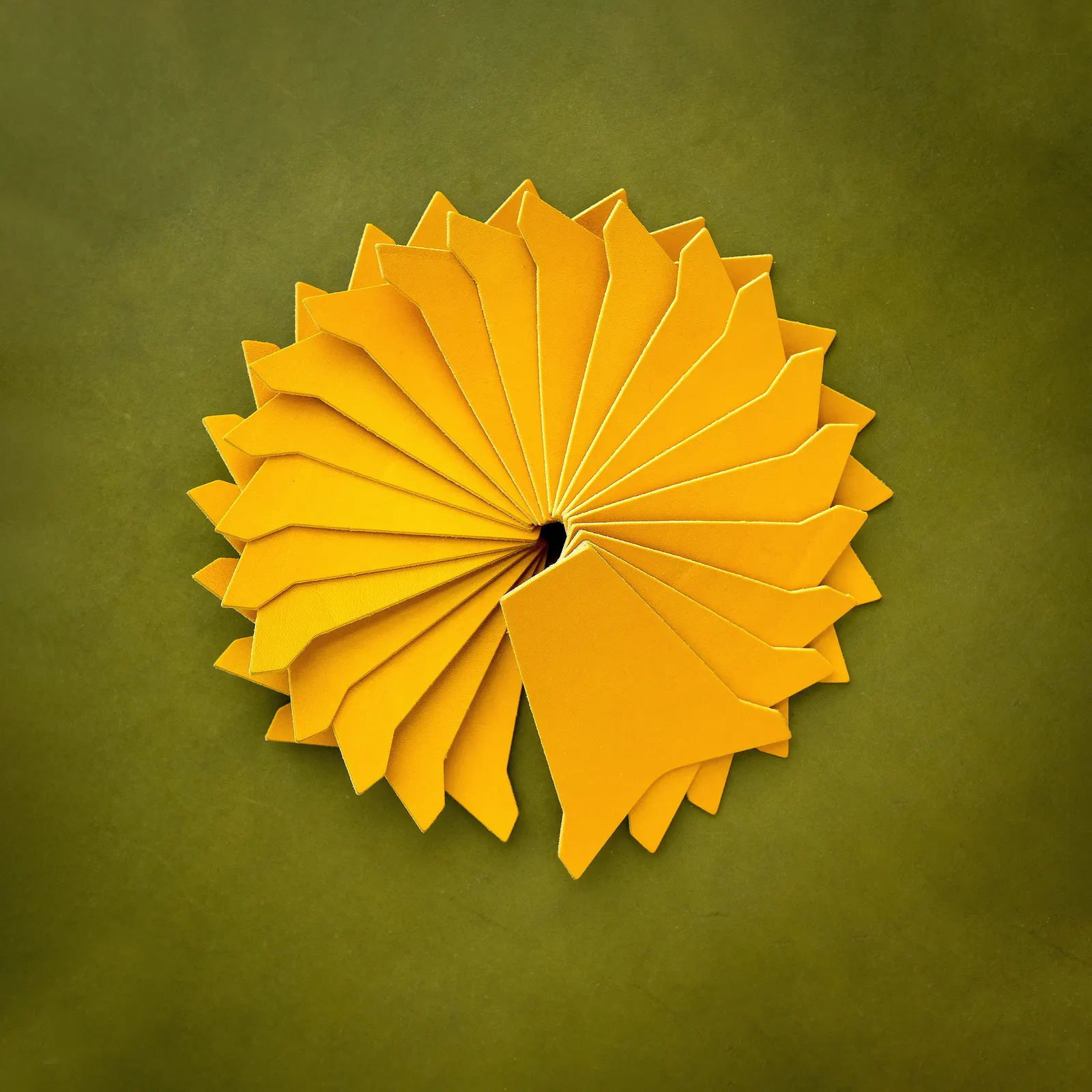 A radial fan of cut yellow leather panels spiraling on an olive backdrop