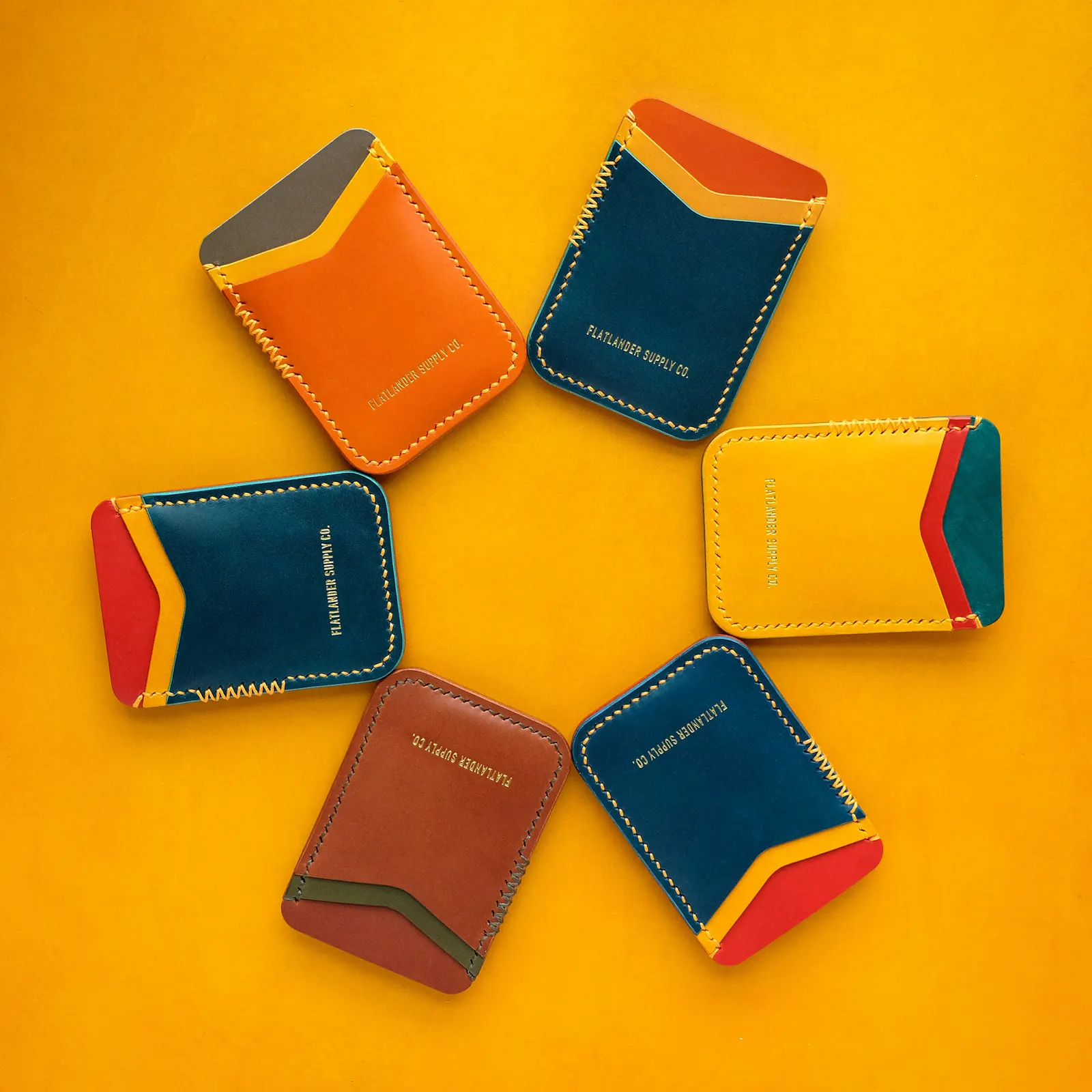 Six card sleeves in mixed colorways arranged in a ring on a yellow leather hide