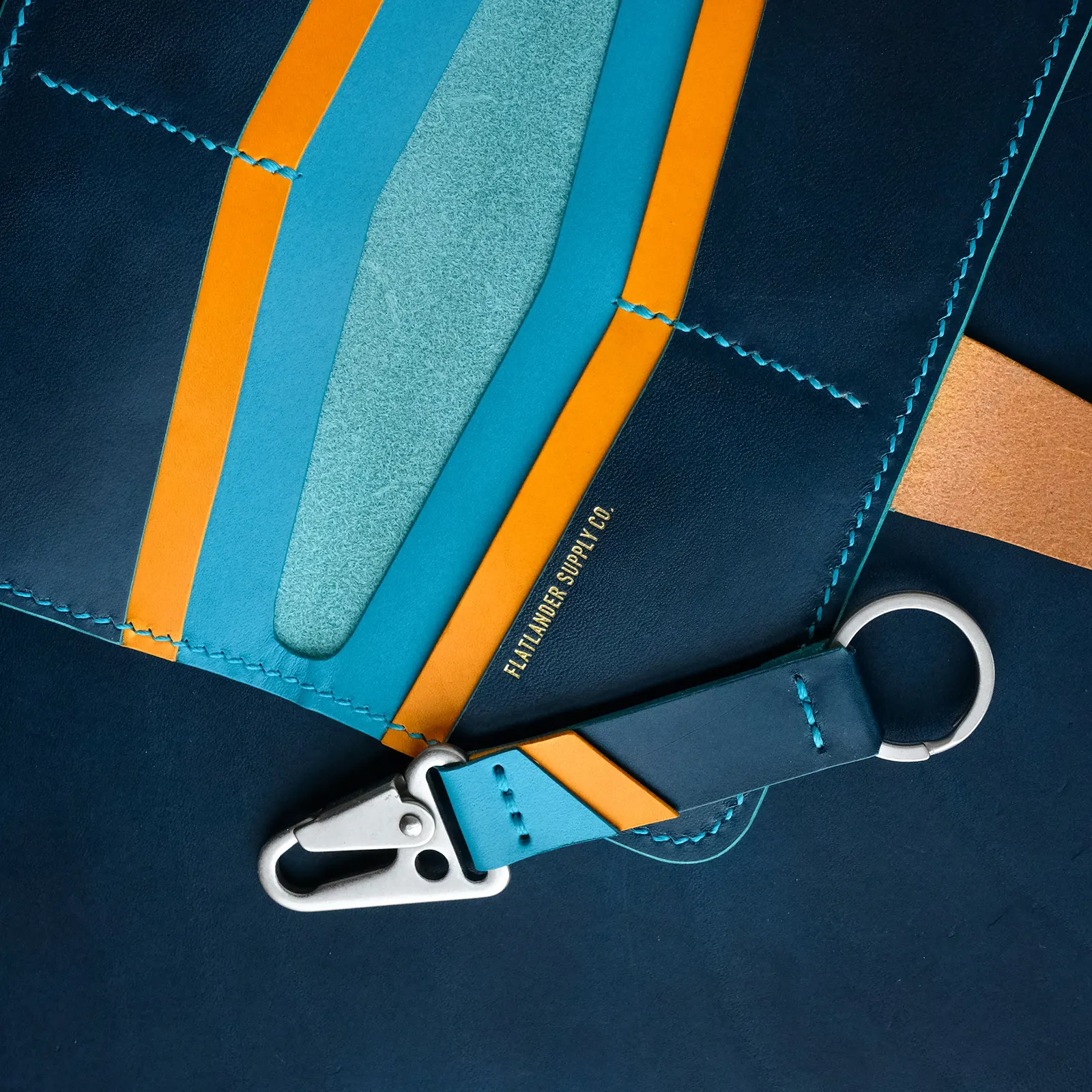 A detail of a navy messenger strap with orange and teal contrast panels, photographed with a keychain clip