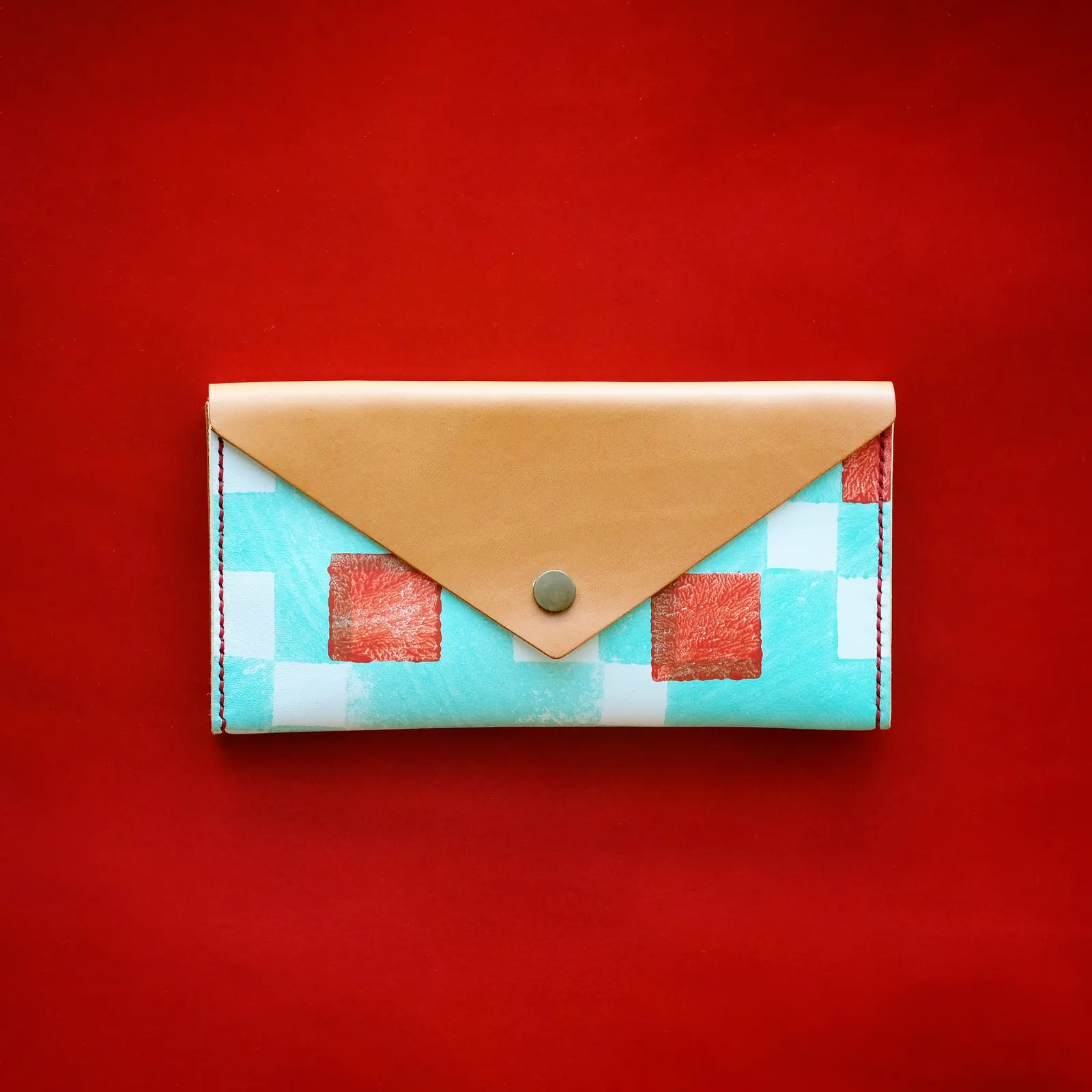 A natural leather and printed-cotton envelope clutch on a red leather hide